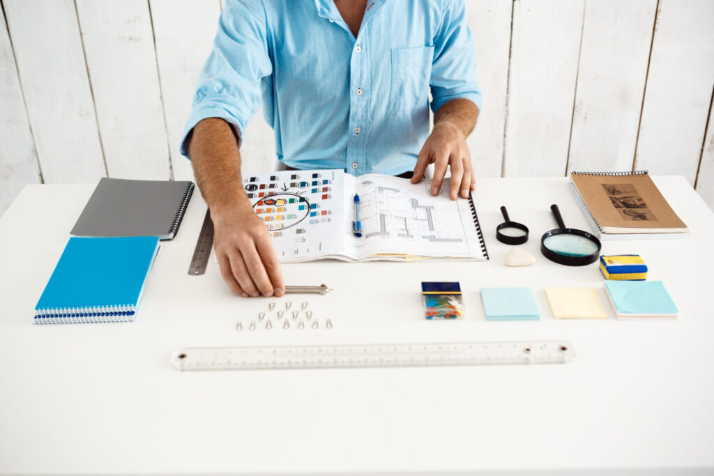 Hands of young businessman sitting at table with notepad. White modern office interior background