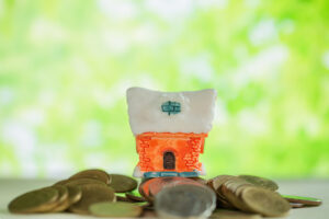 Mini house on stack of coins with green blur background.